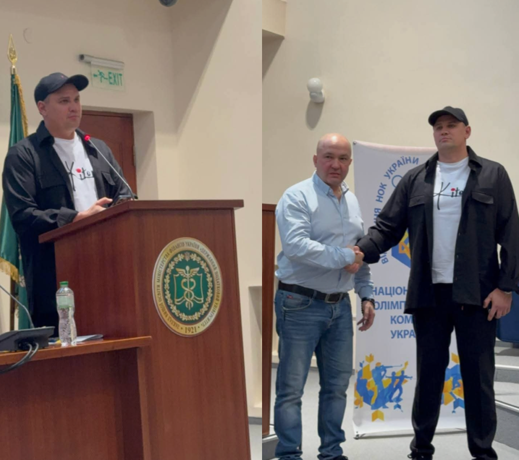 Михайло Уваров в чорній кепці та сорочці виступає за трибуною та тисне руку чоловікові у блакатній сорочці Михайло Уваров в чорній кепці та сорочці виступає за трибуною та тисне руку чоловікові у блакатній сорочці