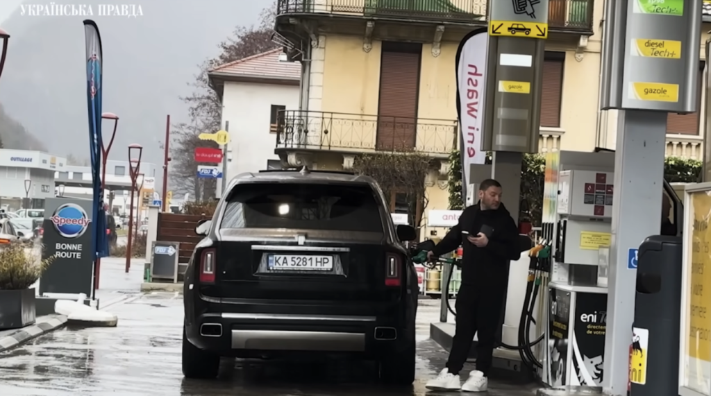 Чоловік в чорному одязі стоїть на автозаправній станції біля чорного автомобіля 